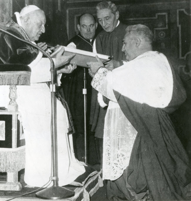 Mgr Pericle Felici, secretaris-generaal van het Concilie, ontvangt uit handen van paus Joannes XXIII de tekst van de apostolische contitutie Humanae Salutis, waarin het Concilie voor het jaar 1962 officieel bijeengeroepen wordt. Tussen de paus en de knielende secretaris zien we Mgr A. van Lierde (links) en Mgr E. Dante (rechts)